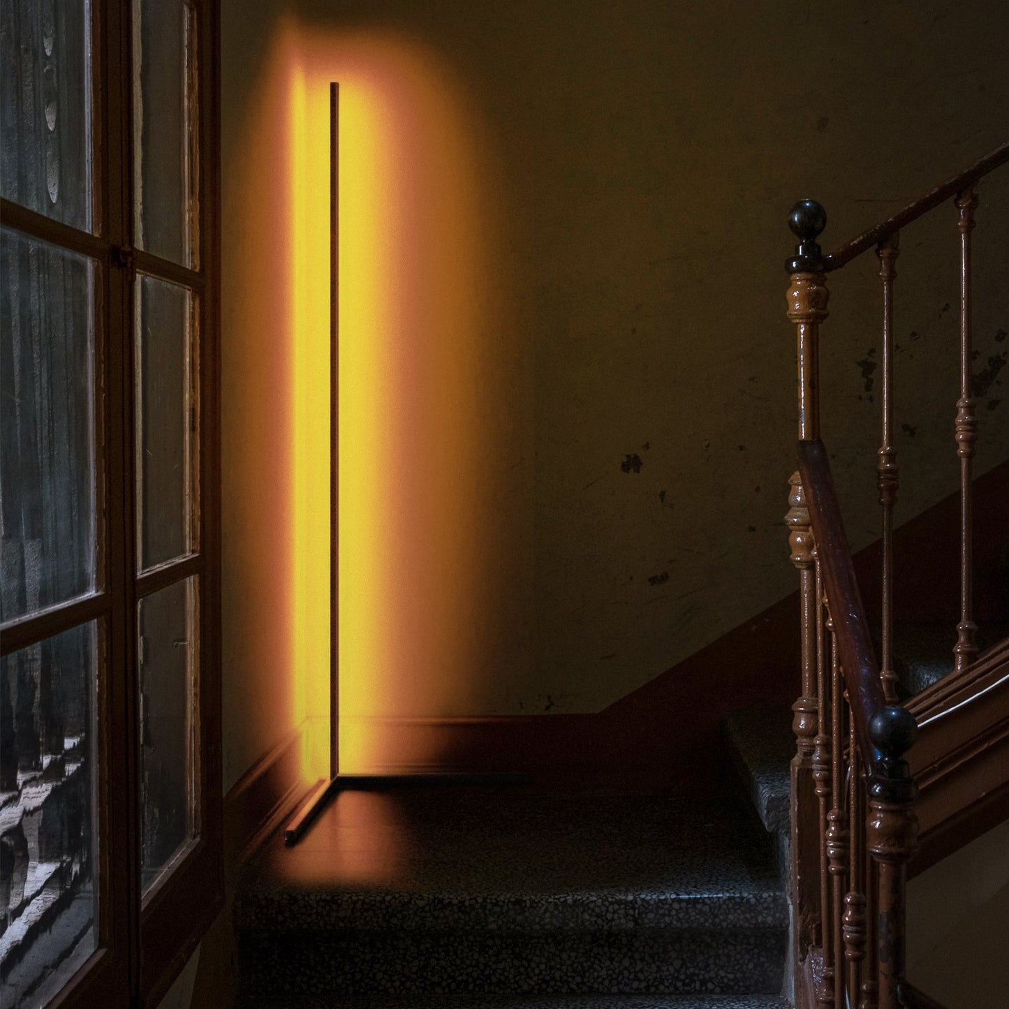 Staircase with a tall, thin floor lamp casting a warm glow against a dark wall.